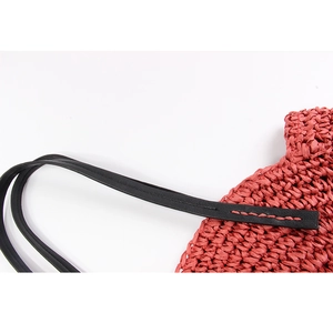 Detail of rose red woven bag featuring black leather strap with red contrast stitching