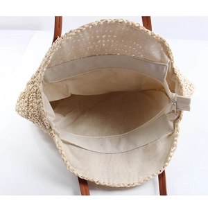 Interior view of round straw bag showing cream lining, zip pocket and metal closure