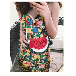 Detail of a handmade crochet watermelon crossbody bag with red pom-poms and thin strap