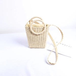 Detail of hand-woven straw bucket bag featuring dual round handles and beige woven strap