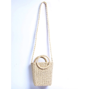 Detail of hand-woven beige straw bucket bag featuring round handles and shoulder strap