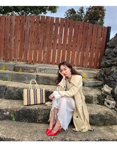 Elegant city outfit featuring a striped straw tote bag and beige trench coat on steps