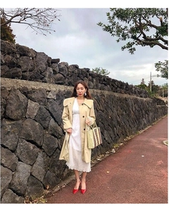 Detail of a large striped straw tote bag paired with a khaki trench coat for beach travel