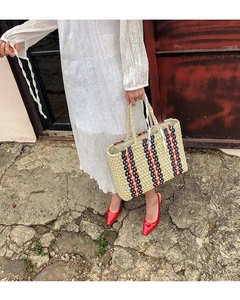 Detail of woven straw tote bag with red and blue stripes held by model in white dress