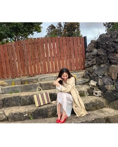 Detail of a large striped straw tote bag paired with a khaki trench coat and red heels