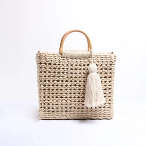 Détail du sac en paille avec anses en bois lisses et pompon de couleur crème