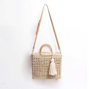 Détail du sac cabas en paille tissé avec anses en cuir et pompon en coton blanc décoratif