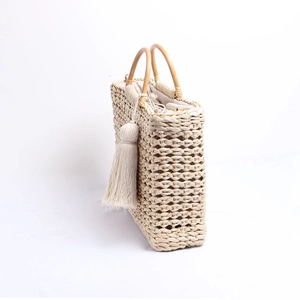 Détail du sac en paille tressée avec poignées en bois et pompon au design ajouré