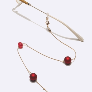Chaîne de lunettes dorée avec perles rouges mates et cristaux sur fond blanc
