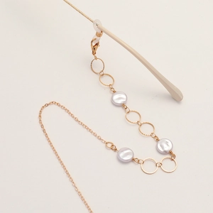 Elegant gold metal glasses chain with pearls and engraved rings on beige background