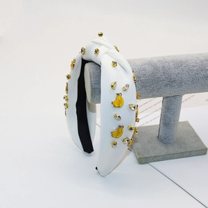 Knotted white fabric headband with banana pendants and crystals on a velvet display stand