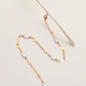 Golden eyewear chain with irregular pearls and round sequins on a beige background
