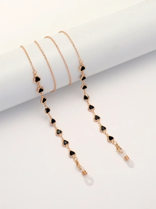 Detailed view of golden metal glasses chain with black heart charms on white display