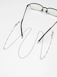 Chaîne à lunettes argentée ornée de perles blanches et boucles en silicone sur fond blanc
