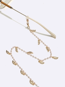 Chaîne de lunettes dorée avec perles blanches et breloques feuilles sur fond blanc