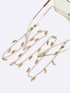 Chaîne de lunettes dorée avec breloques feuilles et perles vue sous un angle de 45 degrés