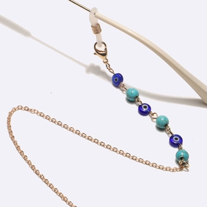 Catenina per occhiali oro con perline turchesi e pendente occhio blu su sfondo bianco
