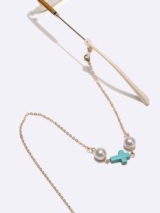 Golden eyewear chain with white pearls and blue cross pendant on a clean white background