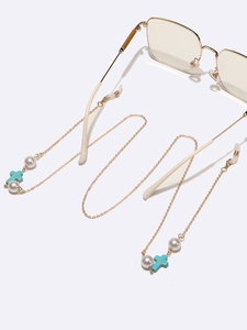 Gold chain glasses strap with white pearls and blue cross charms on white surface