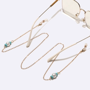 Catenina per occhiali dorata con perle bianche e stelle turchesi su sfondo bianco