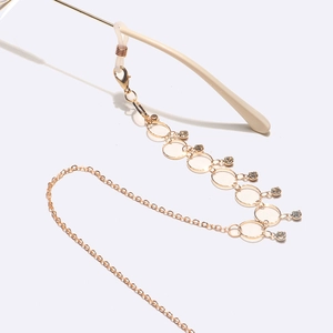 Golden eyewear chain with round link accents and hanging clear rhinestones on white background