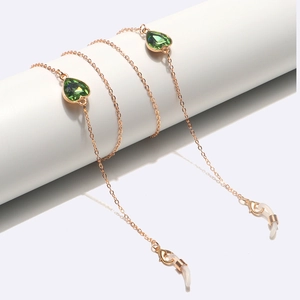 Détail d'une chaîne de lunettes dorée avec cristaux de cœur verts sur un cylindre