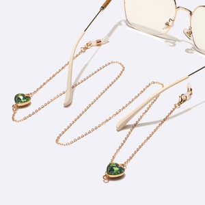 Gros plan d'une chaîne de lunettes dorée avec cristaux de cœur verts et boucles