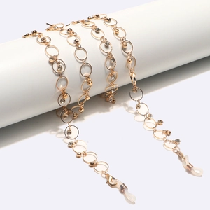Chaîne de lunettes dorée avec strass et maillons circulaires sur support blanc