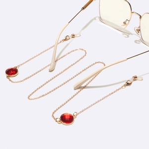 Chaîne de lunettes dorée avec pendentifs en cristal rouge sur fond blanc pur