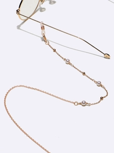 Détail d'une chaîne de lunettes dorée avec perles blanches sur un fond minimaliste