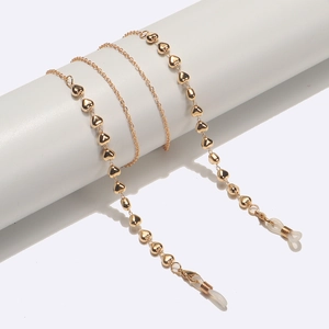 Golden eyewear chain with heart charms and silicone loops on a white display stand