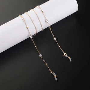 Chaîne de lunettes dorée avec perles blanches sur un support de présentation moderne