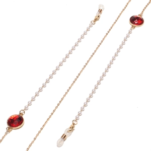 Makro-Detail einer goldenen Brillenkette mit weißen Perlen und facettierten roten Edelsteinen