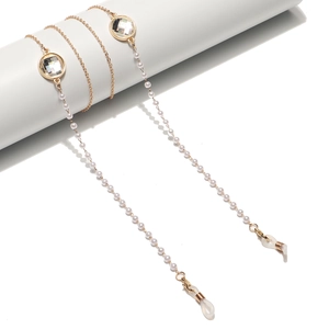 Goldene Brillenkette mit weißen Perlen und großen Kristallen auf weißem Ständer