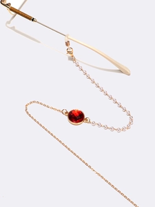Detail einer goldenen Brillen kette mit weißen Perlen und facettiertem rotem Kristall