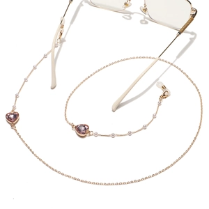 Détail de la chaîne de lunettes dorée avec cristal de cœur rose et perles blanches