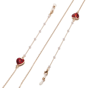 Détail d'une chaîne de lunettes dorée avec perles blanches et deux cœurs rouges