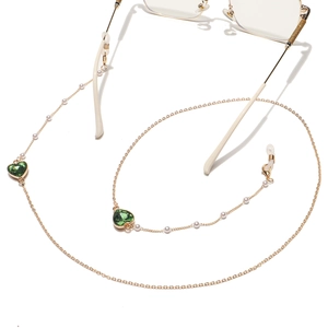Détail de la chaîne de lunettes dorée avec perles blanches et cristaux en cœur vert