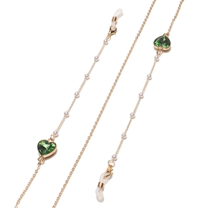Chaîne à lunettes dorée avec perles blanches et cristaux de cœur verts sur fond blanc