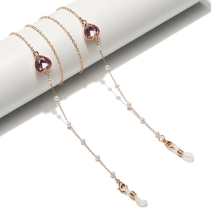 Chaîne de lunettes dorée élégante avec cristaux de cœur roses et perles sur socle blanc