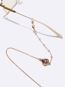 Détail de la chaîne de lunettes en métal doré avec cristal cœur rose et perles blanches
