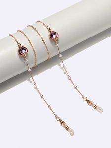 Détail d'une chaîne à lunettes dorée avec coeurs roses et perles sur support blanc