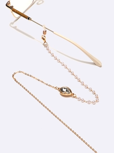 Detail of golden glasses chain with white pearls and a teardrop crystal pendant