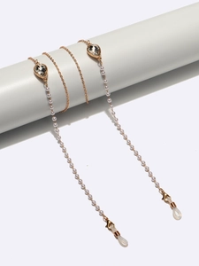 Detail of golden glasses chain with white pearls and teardrop crystals on white display