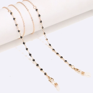 Detail of gold eyewear chain with black rhinestones on a minimalist white stand