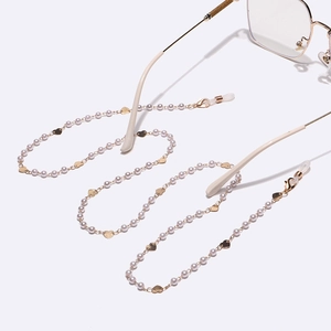 Elegant gold metal eyewear chain with white pearls and heart charms on white background