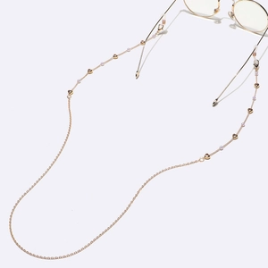 Chaîne à lunettes dorée faite main avec breloques cœurs et perles sur fond blanc