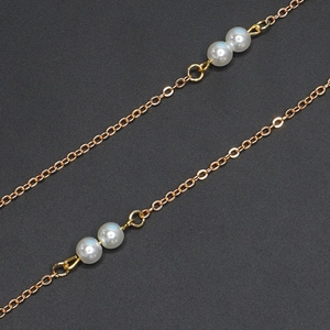 Detailed macro view of thin golden cross-chain featuring elegant white pearl accents