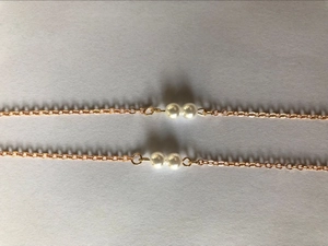 Close-up of golden spectacle chain featuring dual white pearls on a slim metal link