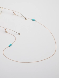 Detail of a gold eyeglasses chain featuring turquoise beads and clear rubber loops